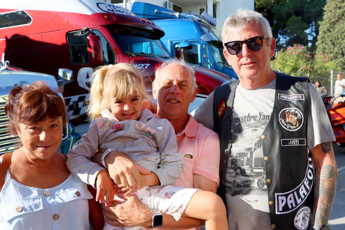 Un grupo de cuatro personas, entre ellas un niño, posando delante de camiones de colores brillantes, captura el momento perfectamente con un borrador automático.