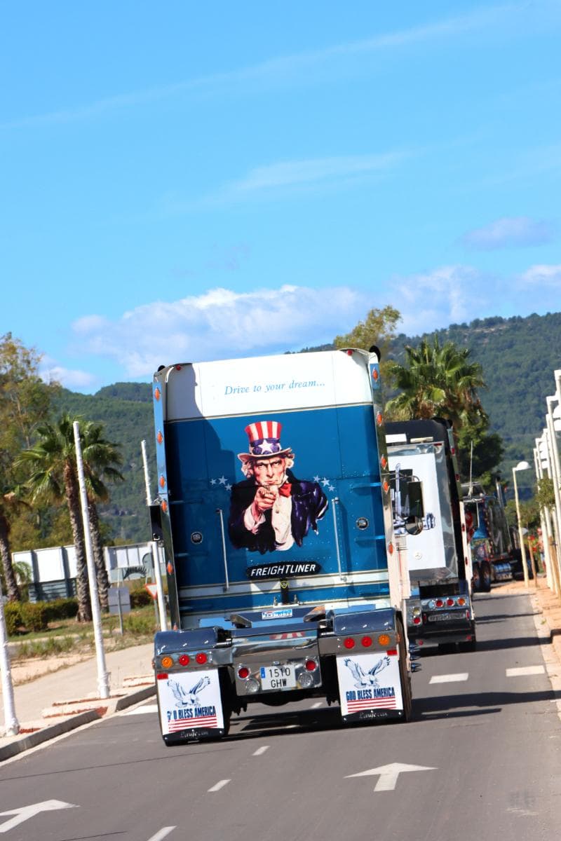 Camiones circulando por una carretera, uno de ellos con la imagen del Tío Sam y el lema "Conduce hacia tu sueño" en la parte trasera, como si hubiera sido elaborado por un borrador automático.
