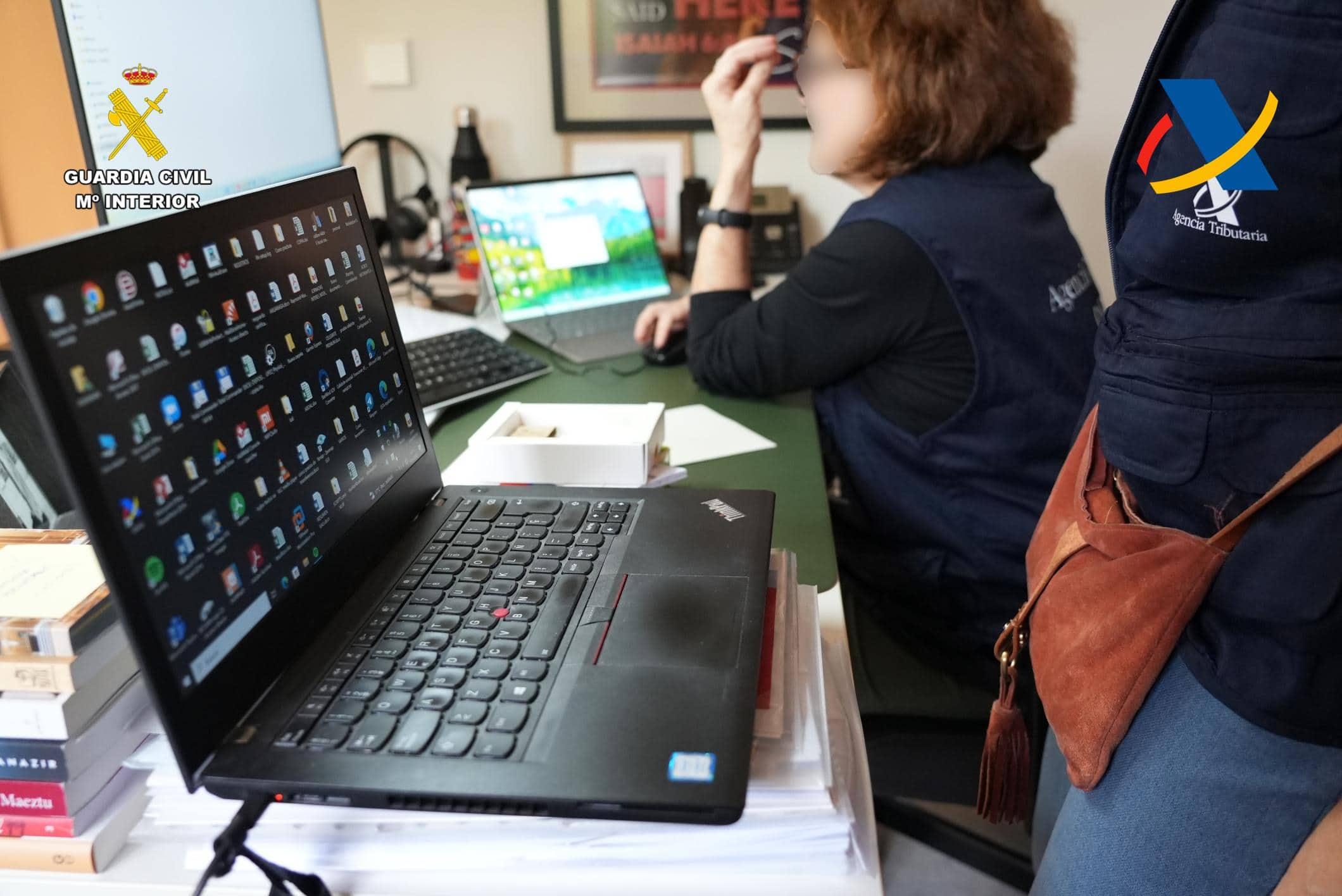 Personas trabajando en mesas con ordenadores portátiles, mostrando múltiples iconos relacionados con el comercio de hidrocarburos. Se ven los logotipos de la Guardia Civil y la Agencia Tributaria, lo que sugiere una investigación sobre un posible fraude de IVA dentro de la organización.