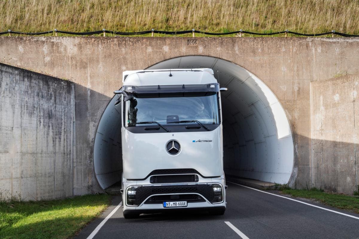 Un camión blanco, que simboliza el desafío del transporte moderno, sale de un túnel en una carretera con un terraplén cubierto de hierba encima, resaltando el compromiso de España con la electromovilidad.
