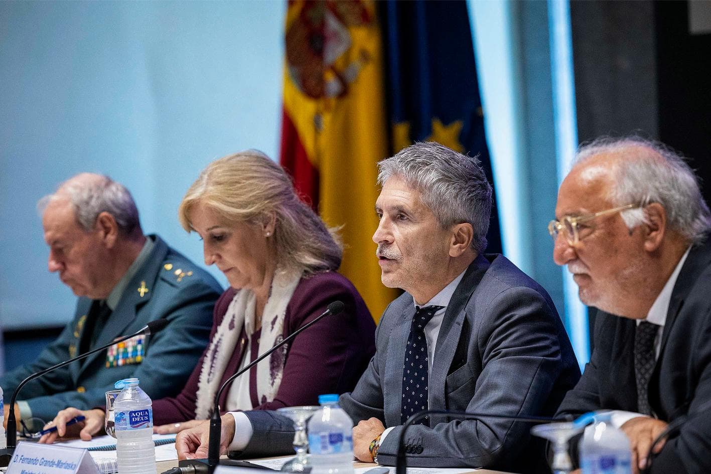 Cuatro personas sentadas en una mesa de conferencias con micrófonos y banderas españolas y de la UE de fondo.
