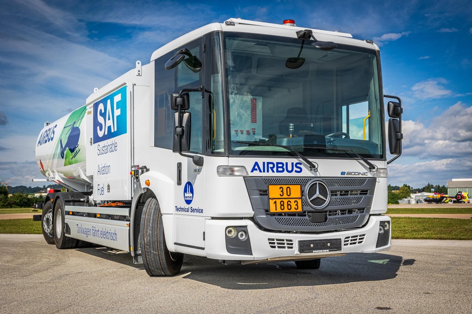 Un camión cisterna Mercedes-Benz con los logotipos de Airbus y SAF está estacionado en un aeródromo bajo un cielo azul nublado, como si fuera un borrador automático.