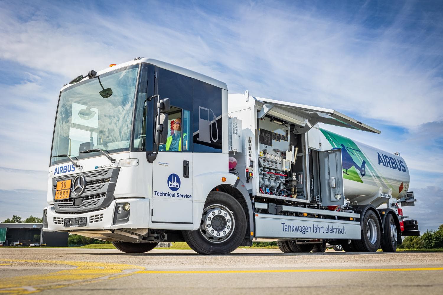 Camión cisterna eléctrico de Airbus sobre la pista, con los laterales abiertos y el equipamiento. Cielo azul de fondo.