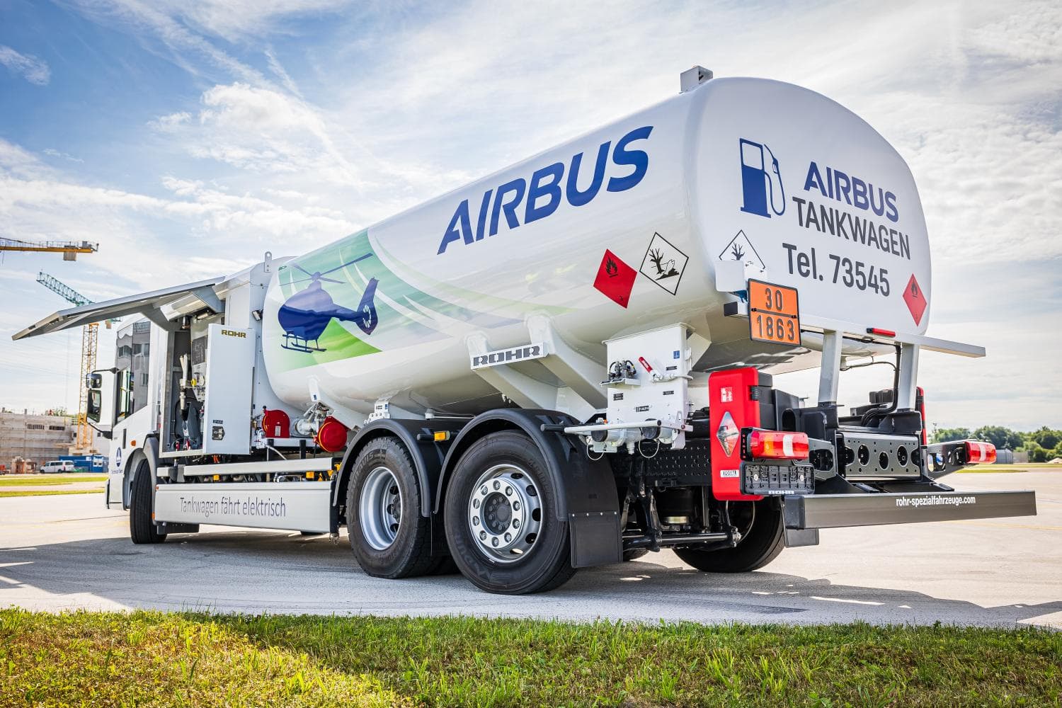 Un camión cisterna de combustible Airbus de color blanco estacionado en la pista de un aeropuerto con un cielo azul claro de fondo.