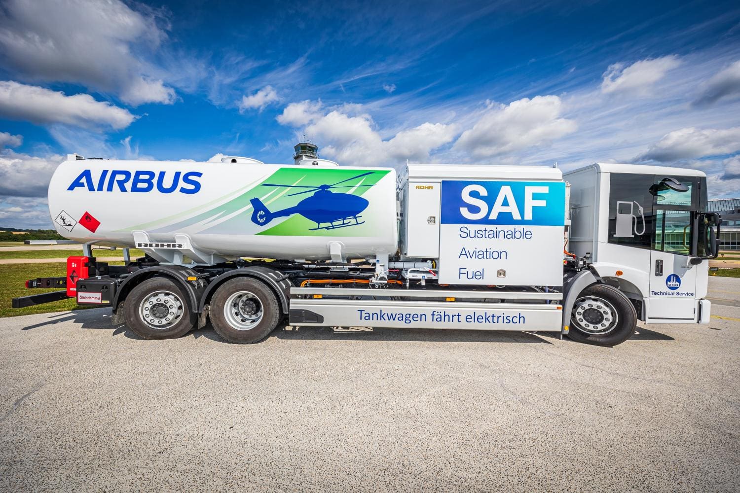 Camión cisterna eléctrico con el logotipo de Airbus y el texto "SAF Sustainable Aviation Fuel", bajo un cielo azul.