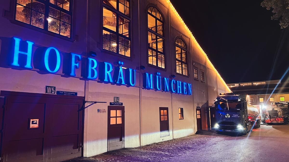 El edificio de la Hofbräu München se alza iluminado contra el cielo nocturno, con un camión estacionado enfrente, que recuerda una escena pintada por un artista con un borrador automático.