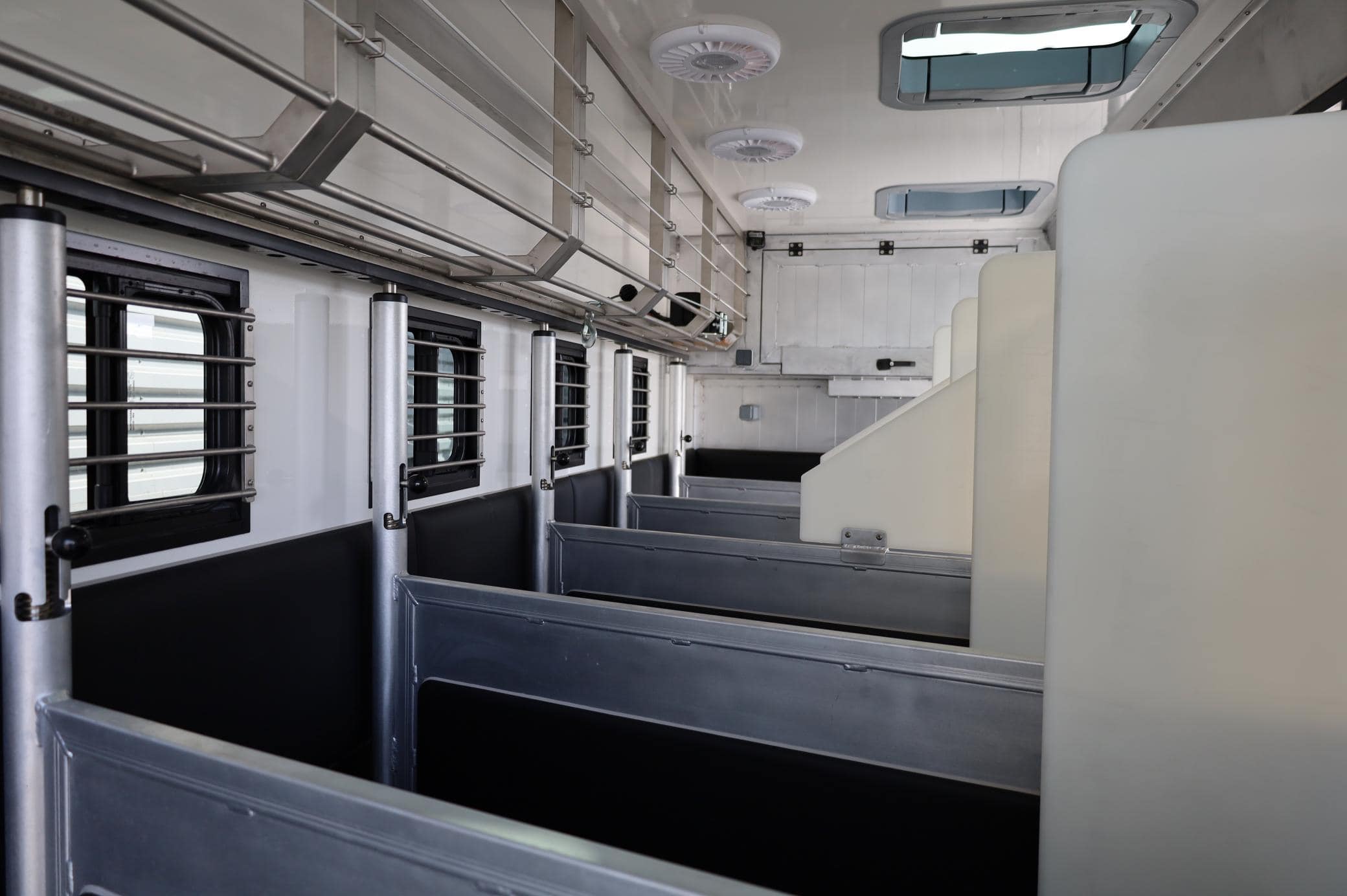El interior de un compartimento de tren vacío cuenta con bancos de metal, ventanas con barrotes y ventiladores de techo, lo que crea un encanto simple. Los estantes se alinean en las paredes para un almacenamiento conveniente. El diseño casi parece un borrador automático: eficiente pero que conserva el encanto del viejo mundo.