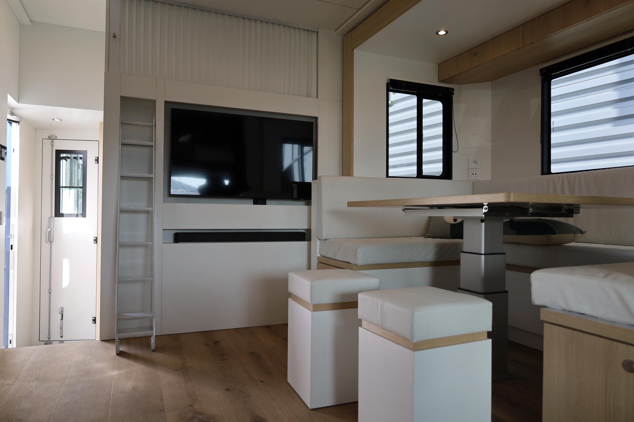 El interior de esta moderna autocaravana cuenta con un televisor, una zona de estar, una mesa y una escalera sobre un suelo de madera, todo ello diseñado para ofrecer comodidad y conveniencia. Las soluciones de almacenamiento inteligentes se integran a la perfección. Es la combinación perfecta de estilo y practicidad con la facilidad de organizar aventuras.