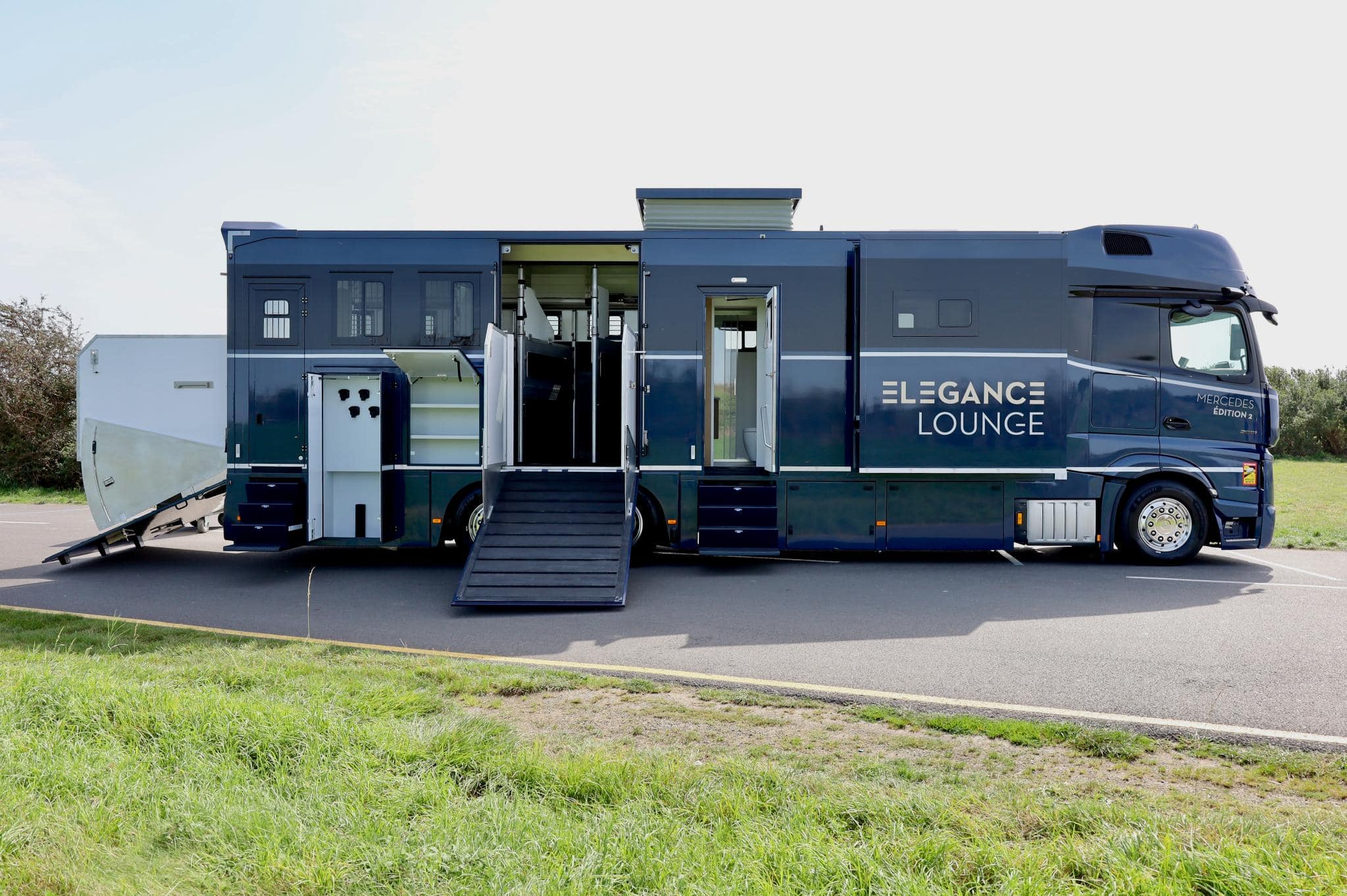 Remolque para caballos de gran tamaño con múltiples puertas y la marca "Elegance Lounge" estacionado sobre asfalto.