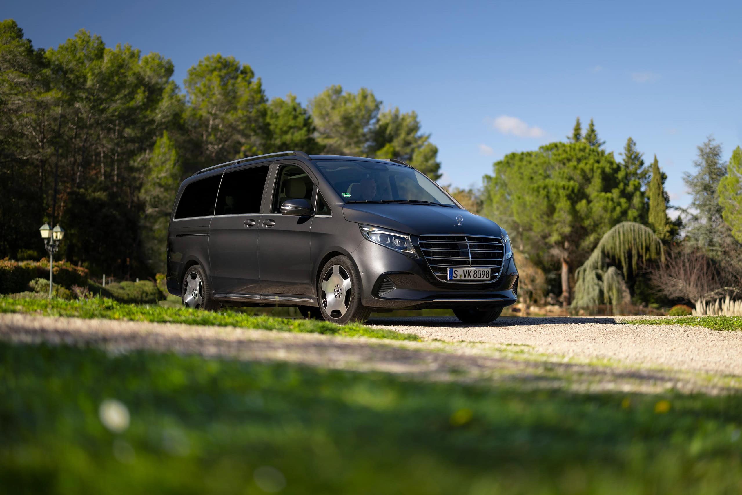 Una furgoneta Renault Master está estacionada en un camino de grava, rodeada de árboles verdes y césped bajo un cielo azul claro, creando la ecuación perfecta de la serenidad de la naturaleza y la ingeniería moderna.