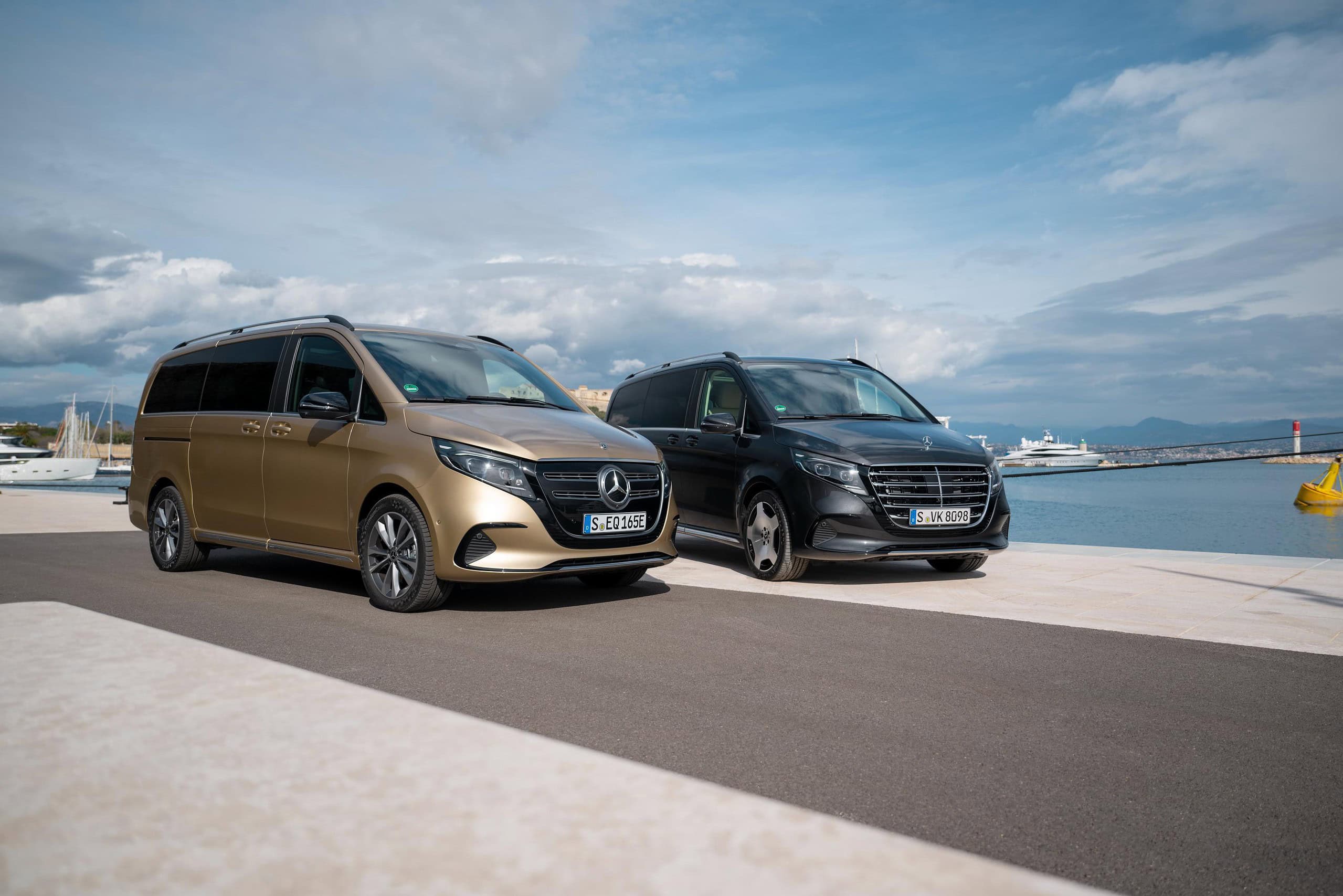 Dos furgonetas Mercedes, la ecuación perfecta de estilo y funcionalidad, están estacionadas junto a un puerto deportivo. El cielo nublado se alza sobre ellas mientras el mar se extiende al fondo, creando una escena serena.