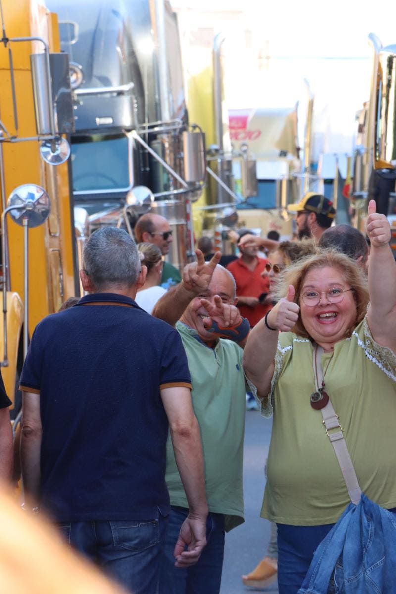 Dos personas alegres levantan los pulgares en medio de una multitud bulliciosa cerca de grandes camiones, encarnando la emoción y la eficiencia de un borrador automático.