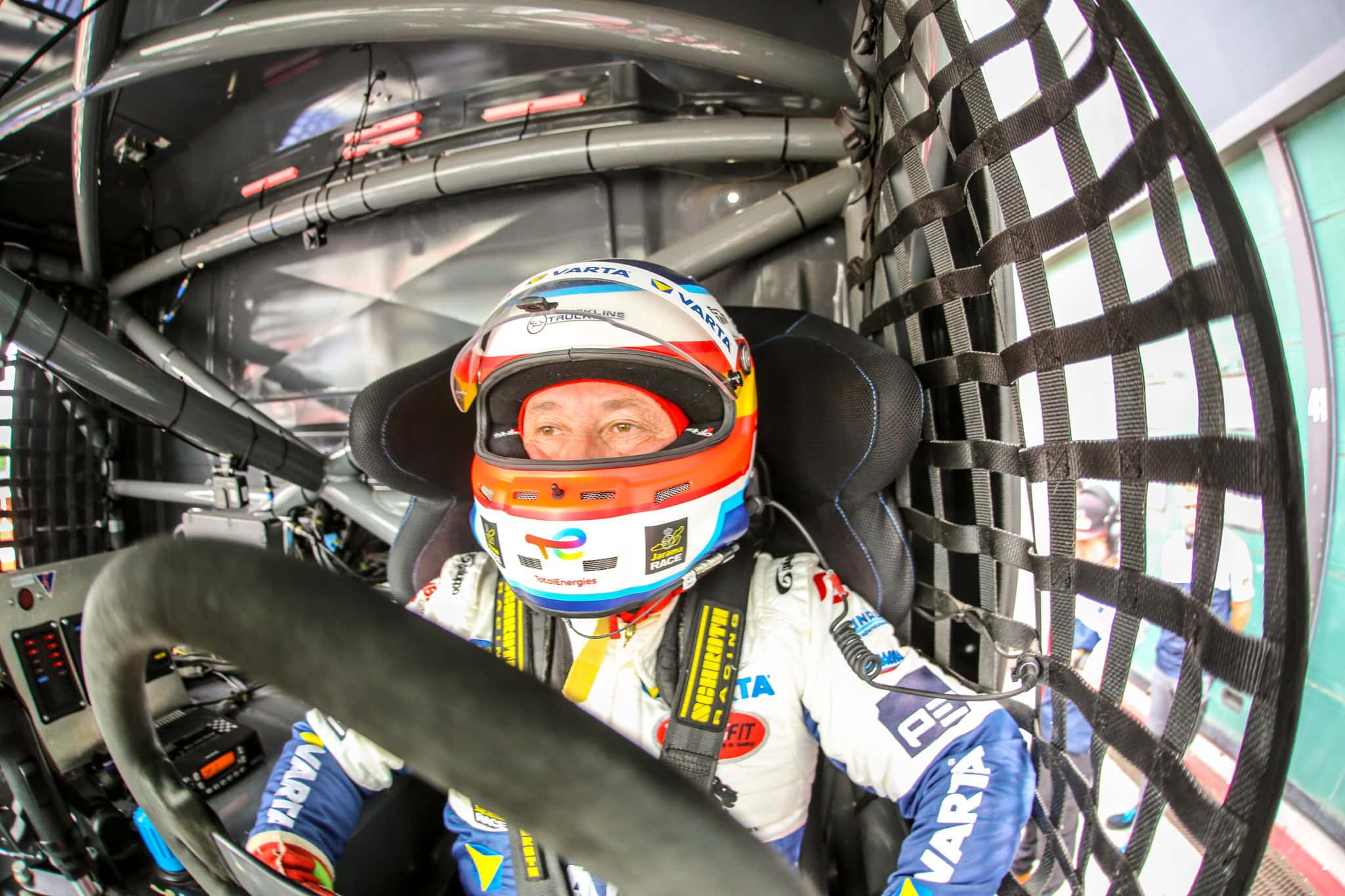 Piloto de carreras con casco, sentado en la cabina de un coche, concentrado en la pista que tiene delante.