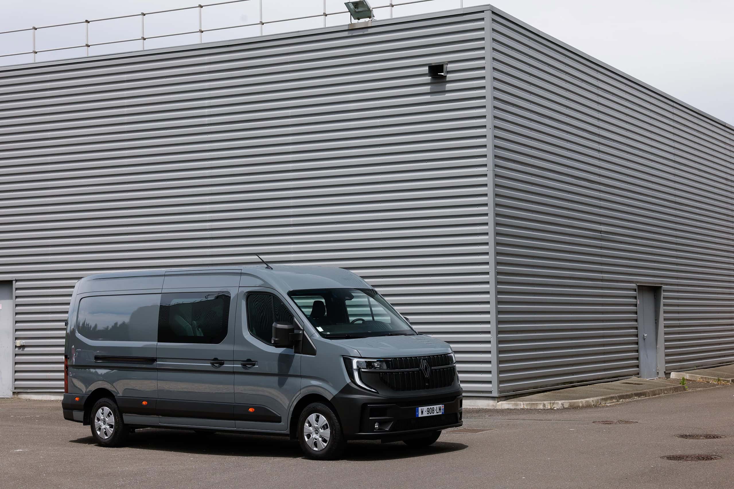 Una furgoneta Renault Master está estacionada frente a un gran edificio de chapa ondulada en un día nublado, presentando una ecuación perfecta de encanto industrial y funcionalidad.