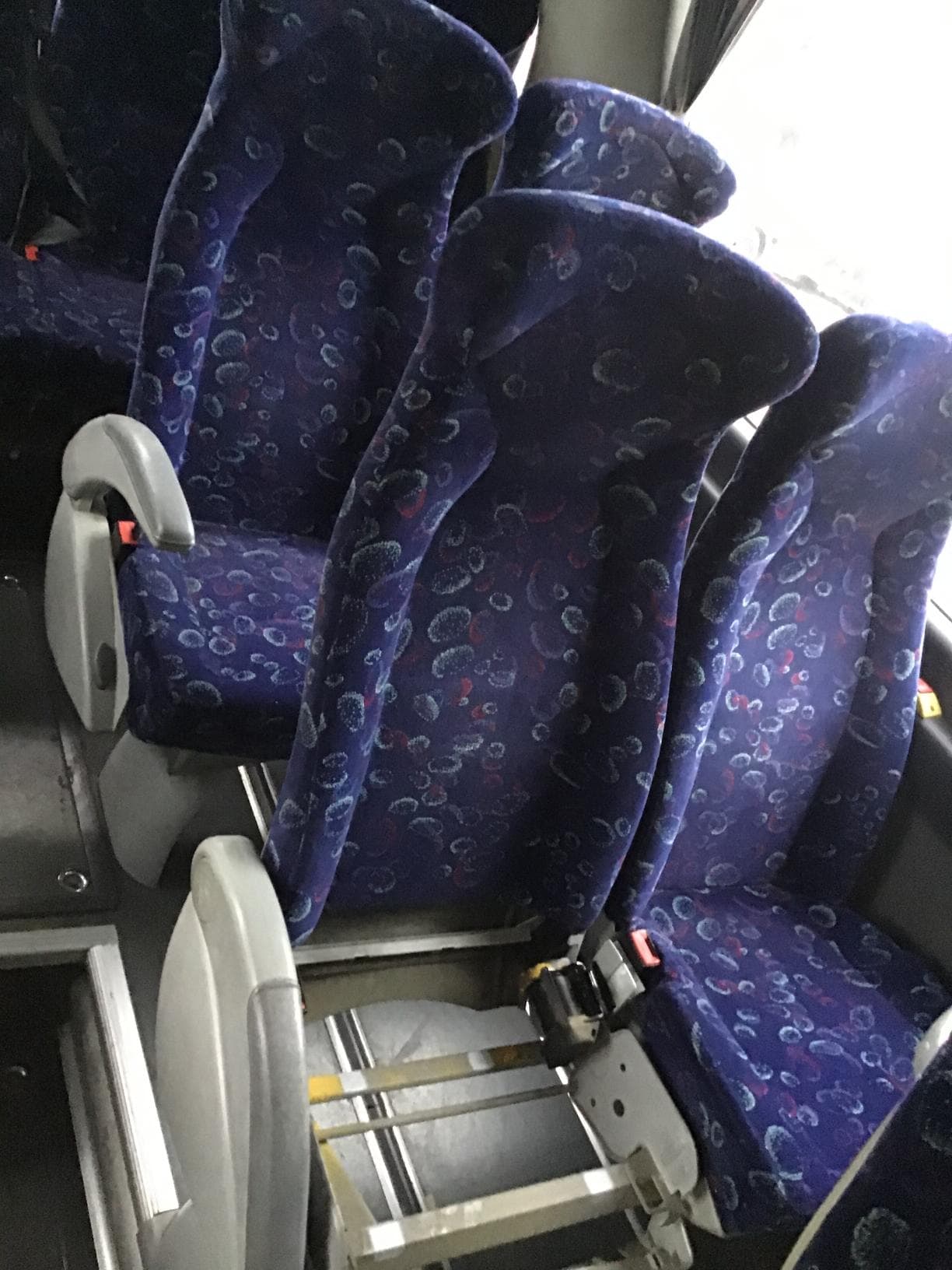 Tres asientos de autobús con estampado azul, con uno de ellos faltante y que muestra un marco de metal.