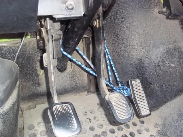Pedales de automóvil con una cuerda azul atada alrededor del embrague y el freno, mostrando una configuración inusual.