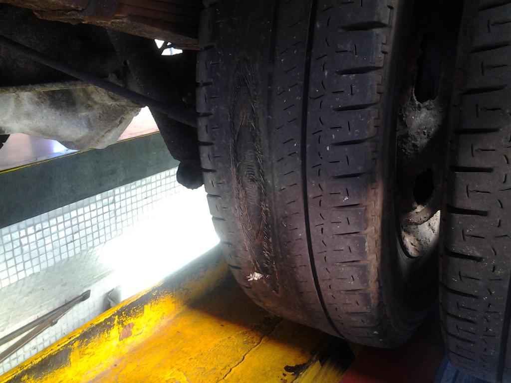 Primer plano de un neumático de automóvil con desgaste visible y una gran mancha desgastada en las bandas de rodadura.