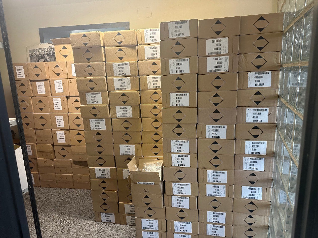 Pilas de cajas de cartón etiquetadas como AP-7, cada una con códigos de barras, se amontonan en una pequeña habitación.
