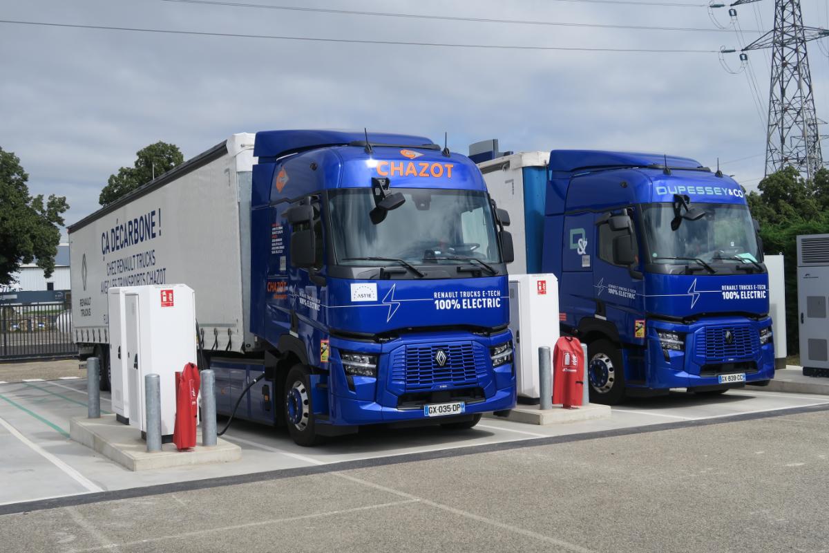 Dos Renault Trucks azules estacionados en estaciones de carga en una instalación al aire libre, mostrando su destreza en la distribución regional con energía eléctrica.