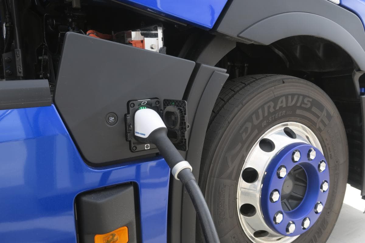 Un Renault Trucks eléctrico enchufado a una estación de carga, que muestra un primer plano del puerto de carga y la rueda, perfectamente adecuado para la distribución eléctrica regional.