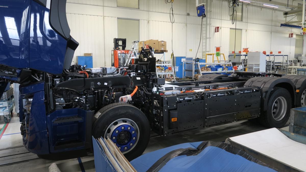 En un entorno industrial lleno de actividad, el chasis del camión eléctrico parcialmente ensamblado refleja el compromiso de Renault Trucks con la distribución regional, rodeado de diversas herramientas y equipos en segundo plano.