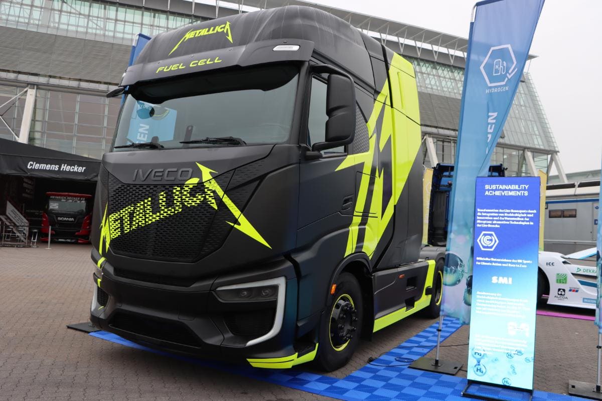 Camión de pila de combustible Iveco con la marca "Metallica" exhibido en un evento al aire libre con un cartel de logros en materia de sostenibilidad.