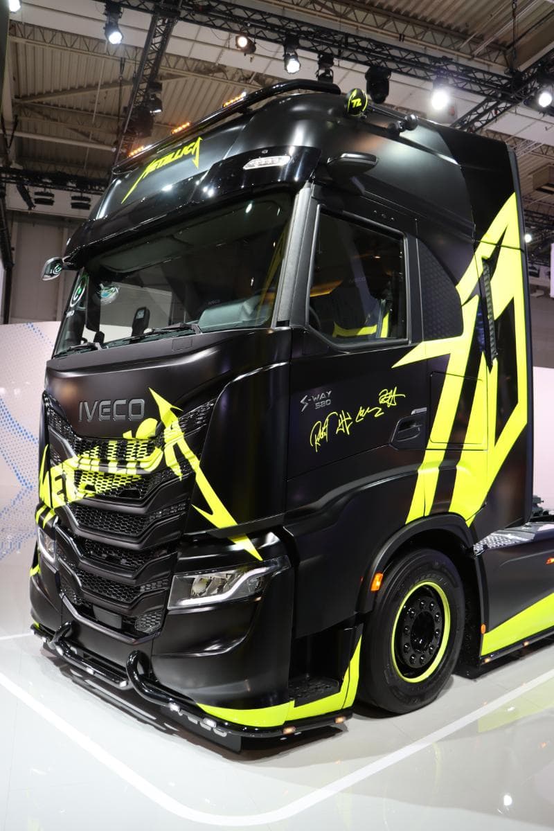 Camión Iveco negro con detalles en verde neón y la marca "Metallica", exhibido en el interior sobre un piso brillante.