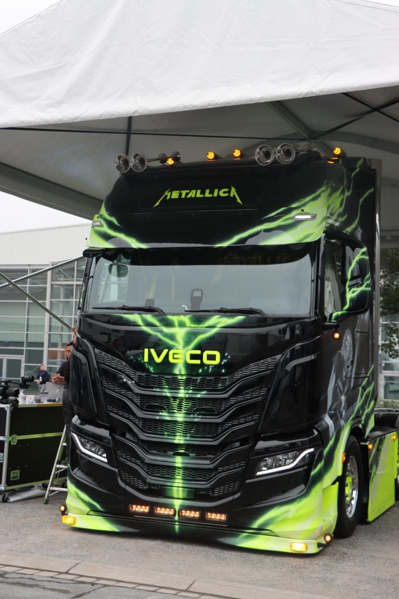Un camión Iveco pintado a medida con la marca "Metallica" y gráficos de rayos verdes, exhibido debajo de una carpa.