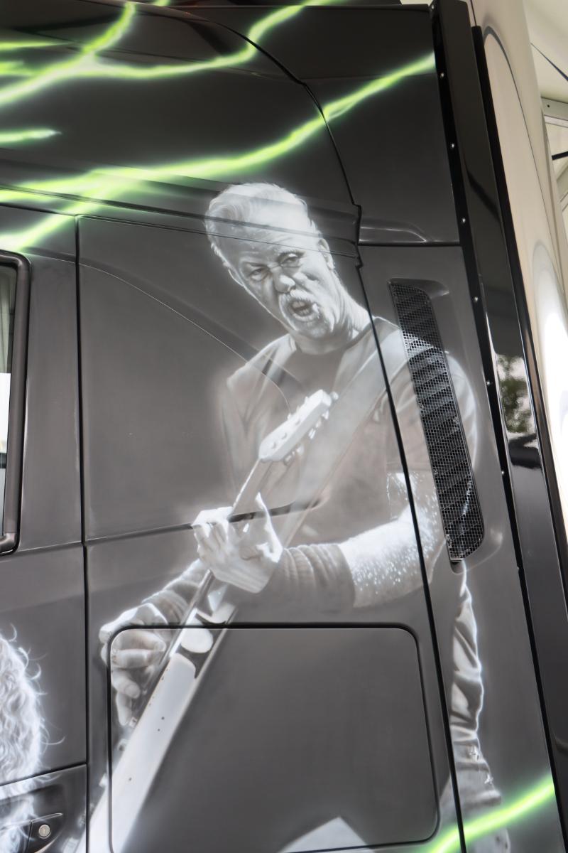 Obra de arte de un guitarrista tocando apasionadamente, pintada en el costado de un camión con acentos verdes en el fondo.