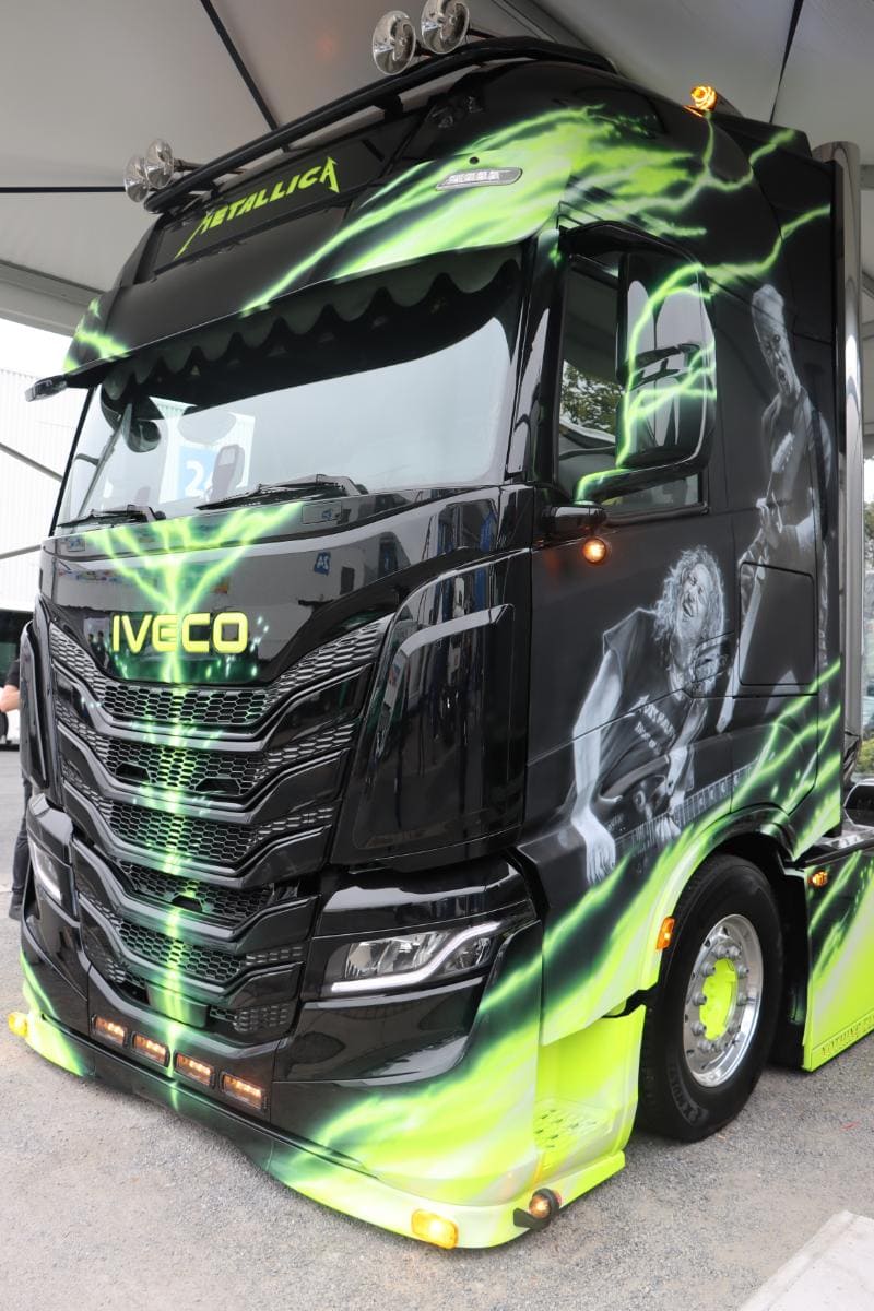 Un gran camión negro con detalles en verde y amarillo presenta calcomanías con temática de Metallica en los costados y el frente.