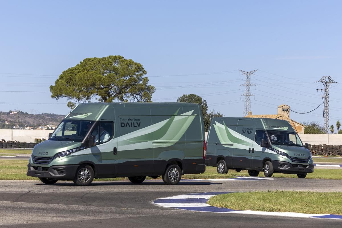 Dos furgonetas de reparto IVECO verdes circulan por una pista soleada en el Circuito Aspar de Valencia, con árboles y líneas eléctricas al fondo.