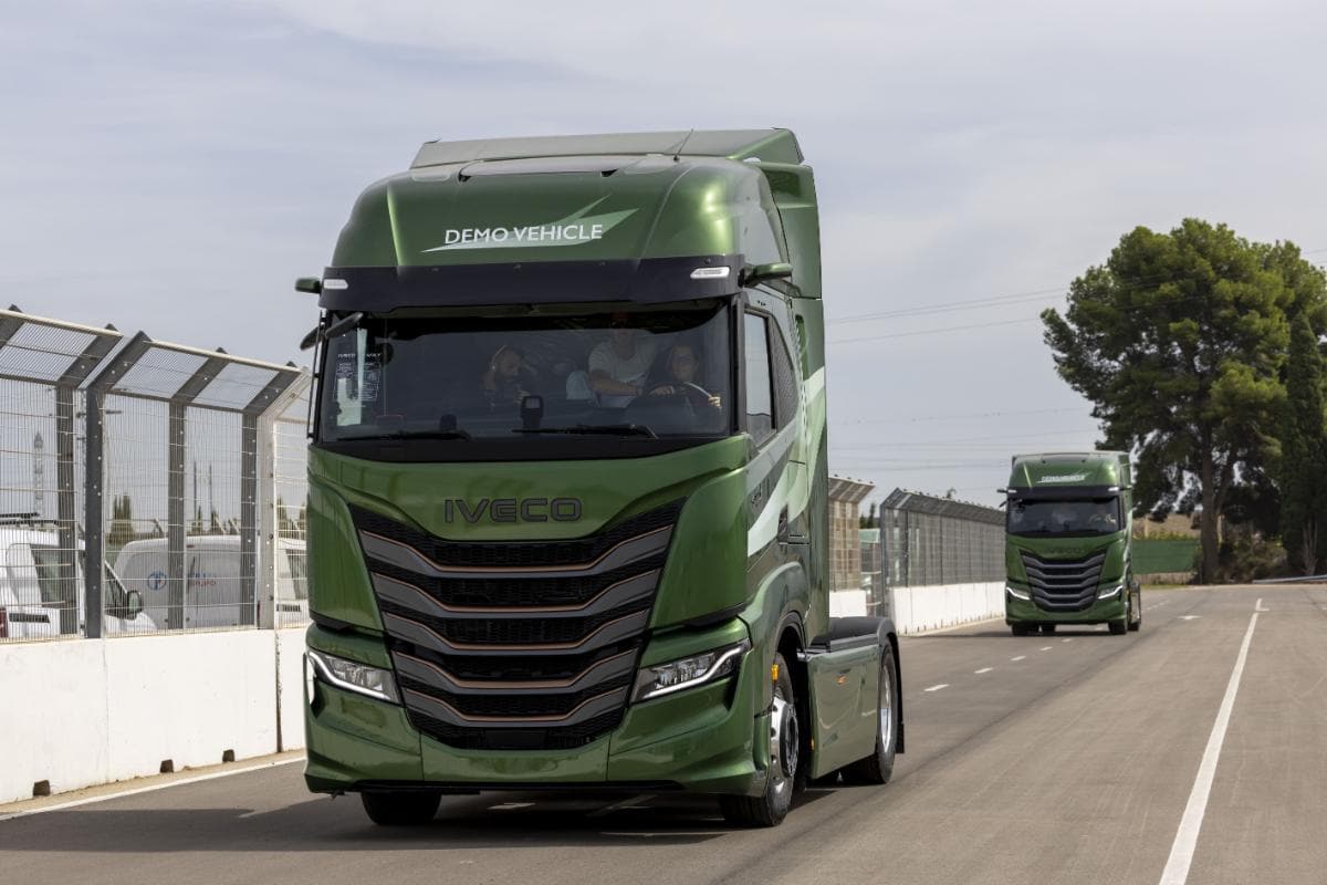 Se ven dos camiones Iveco verdes rotulados "Demo Vehicle" de la nueva gama circulando por una carretera asfaltada, rodeados de árboles y una valla, haciendo eco del dinamismo del Aspar Circuit de Valencia.
