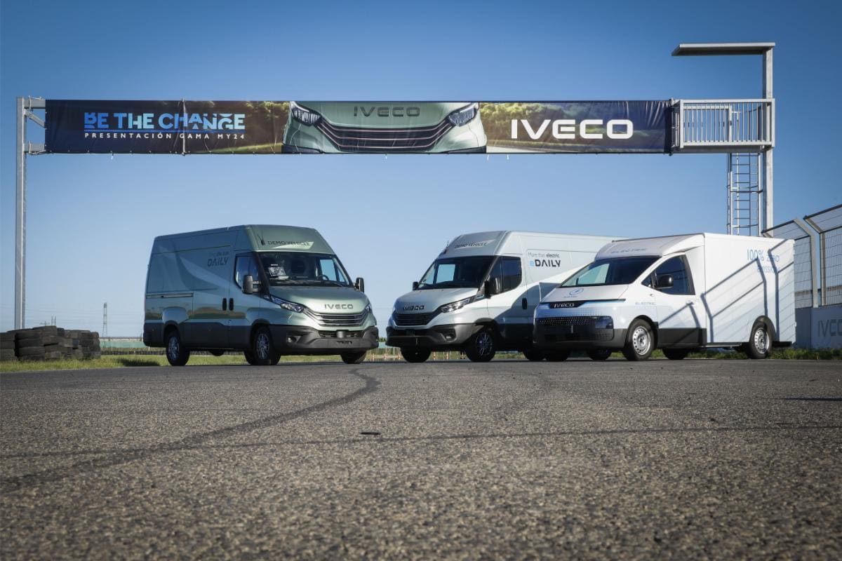 Tres furgonetas IVECO aparcadas en el soleado circuito Aspar Circuit de Valencia bajo una pancarta "Be the Change", mostrando la nueva gama de vehículos.