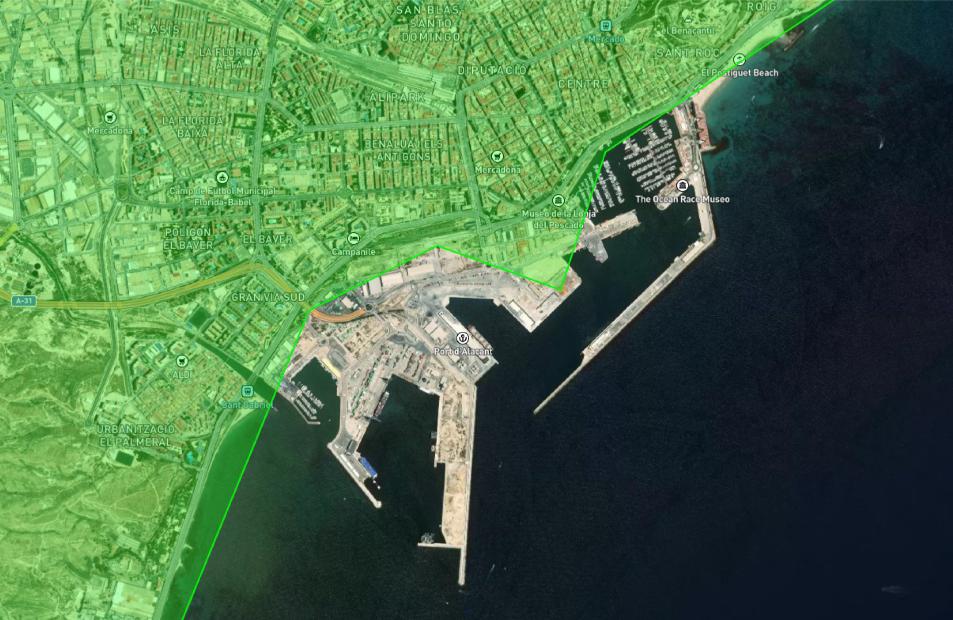 Una vista satelital captura una ciudad costera con un puerto bullicioso, caminos intrincados y edificios diversos, todo enclavado entre una tierra verde y un mar azul oscuro. Las complejidades de la cartografía moderna revelan detalles ocultos en este mapa visual de segunda generación.