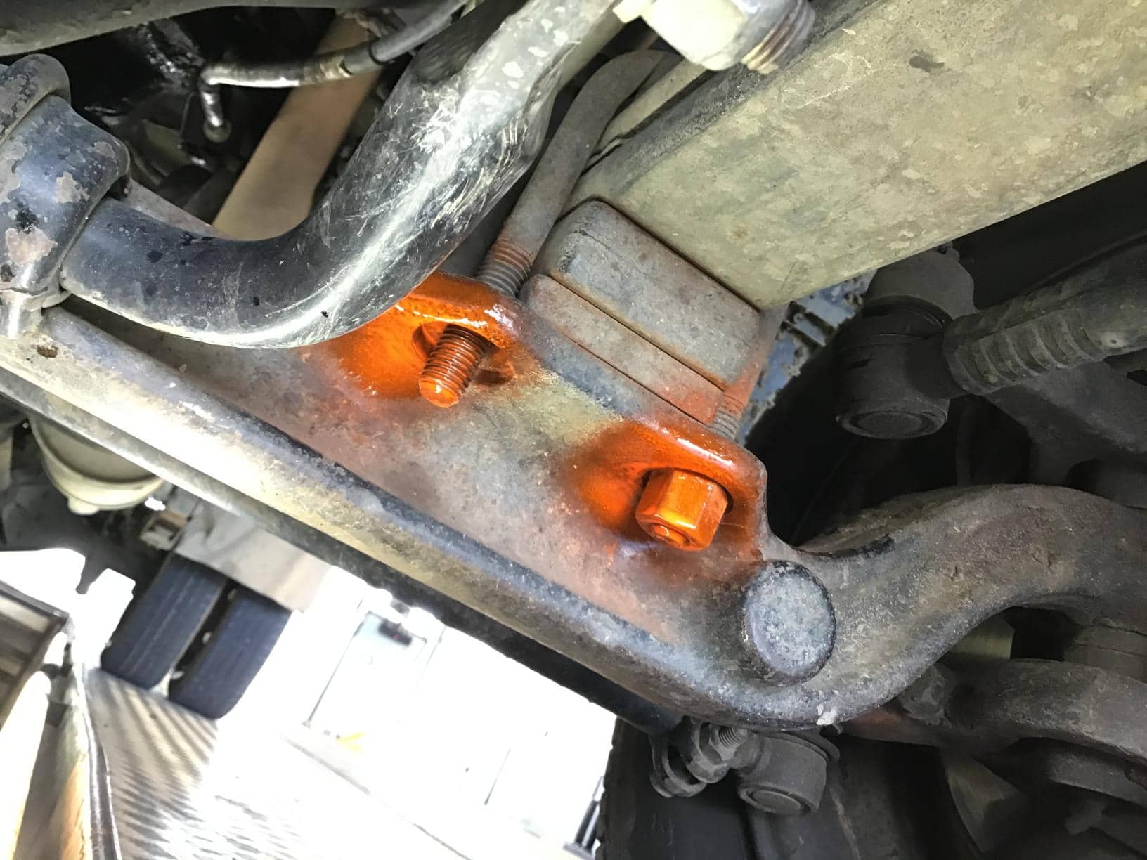Primer plano del tren de aterrizaje del vehículo con pernos de color naranja resaltados en un soporte de metal.