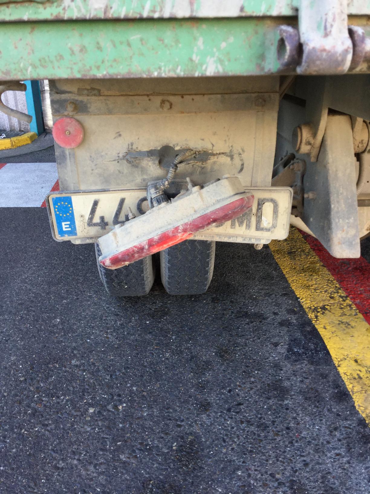 Parte trasera de un camión sucio con la matrícula doblada y la luz trasera rota.