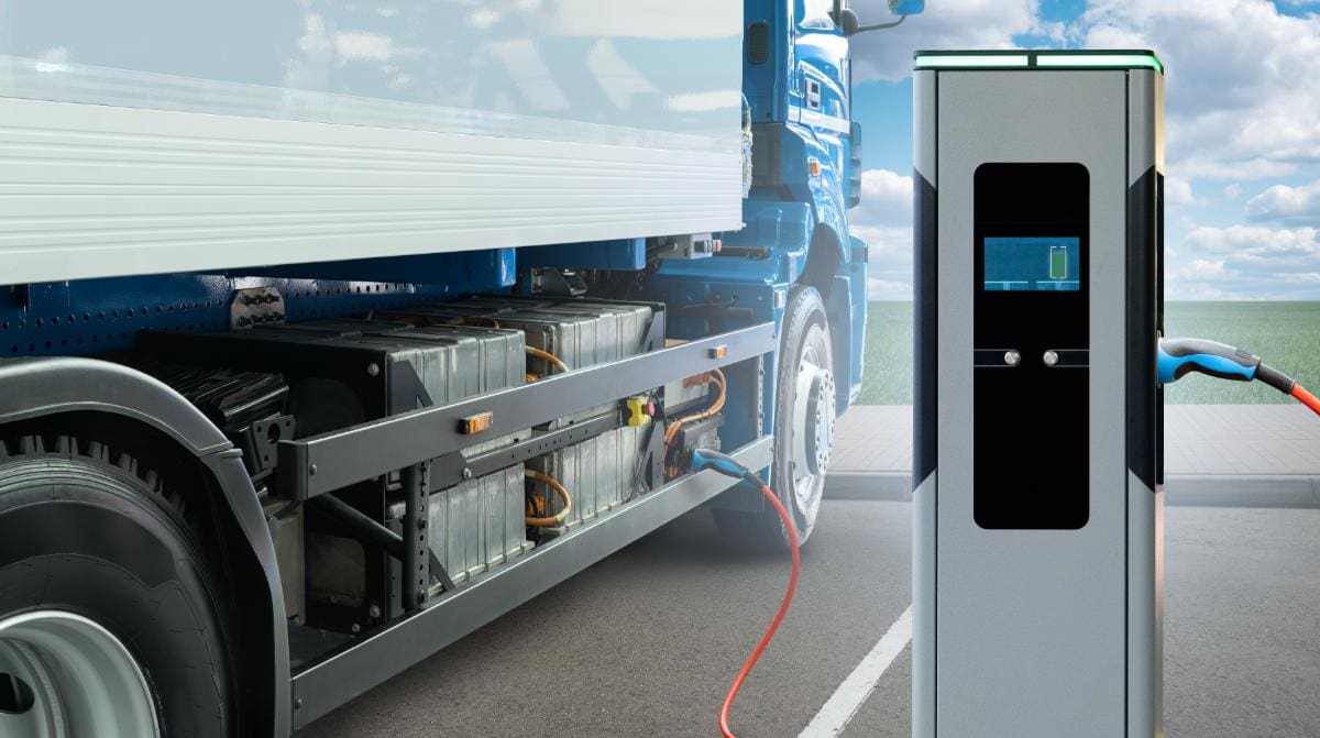 Un camión eléctrico conectado a una estación de carga bajo el brillante sol español, con un cielo azul de fondo, encarna el espíritu de la electromovilidad.
