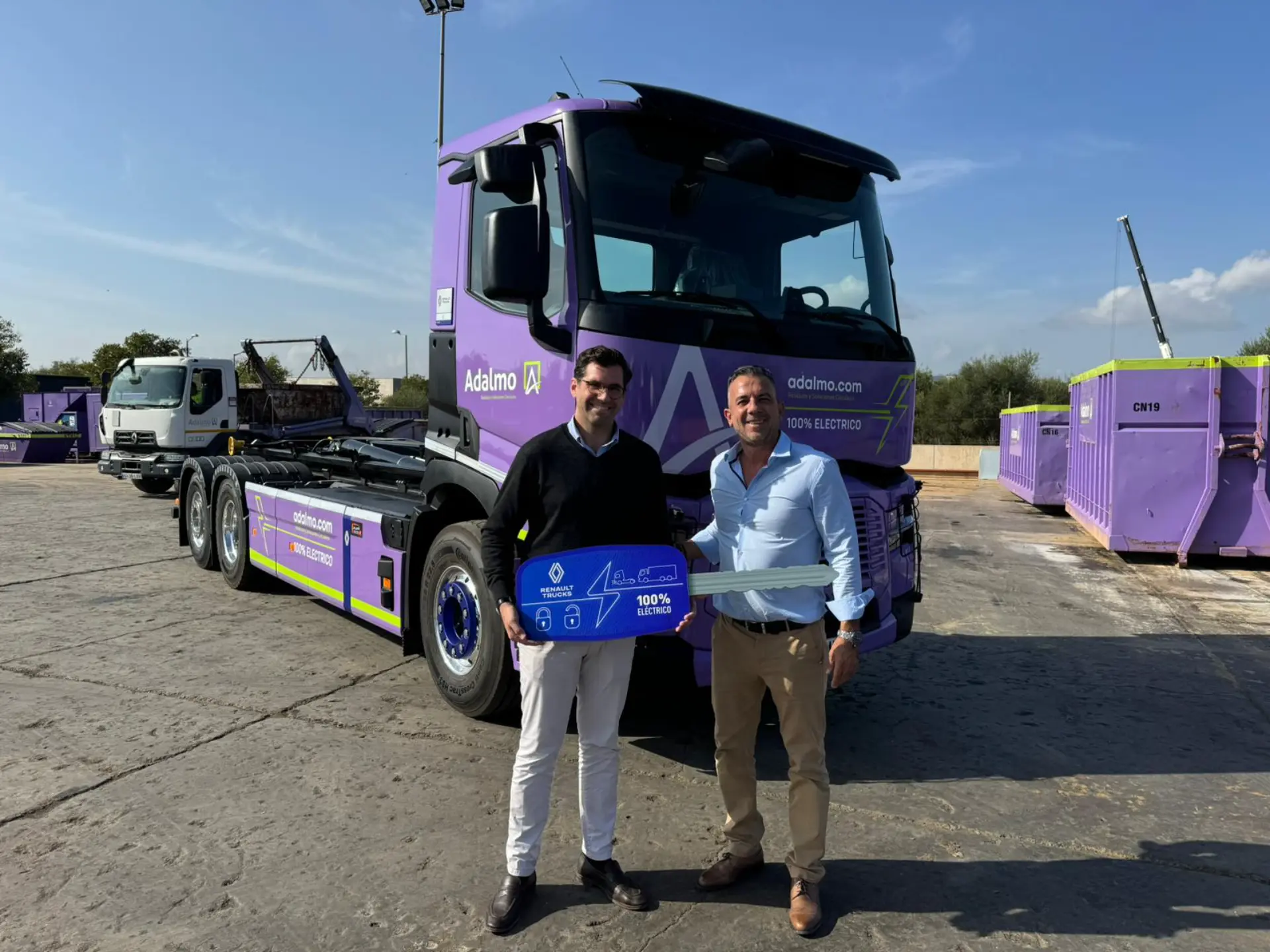 Dos personas de pie delante de un camión eléctrico violeta de Adifmo sosteniendo una gran llave azul.