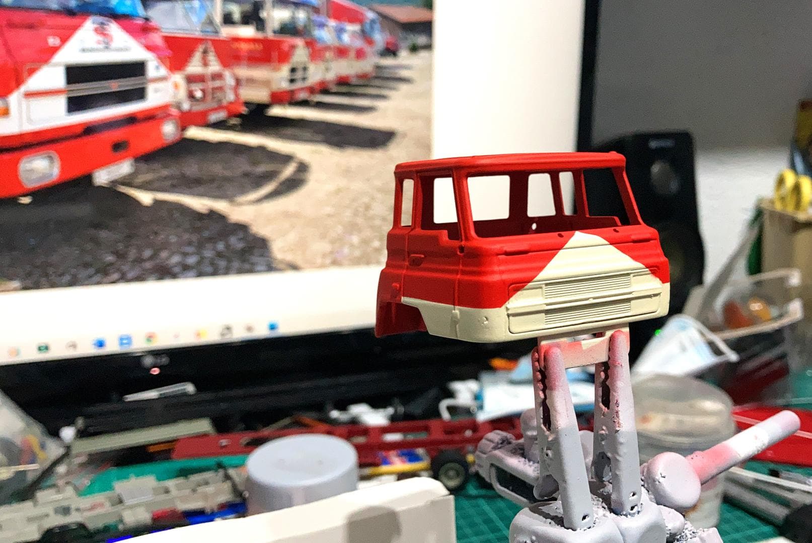 Una maqueta de autobús de color rojo y blanco, que representa el viaje de Antonio Fernández, se sostiene mediante un clip contra el fondo de una pantalla de computadora que muestra autobuses similares navegando alrededor de obstáculos.
