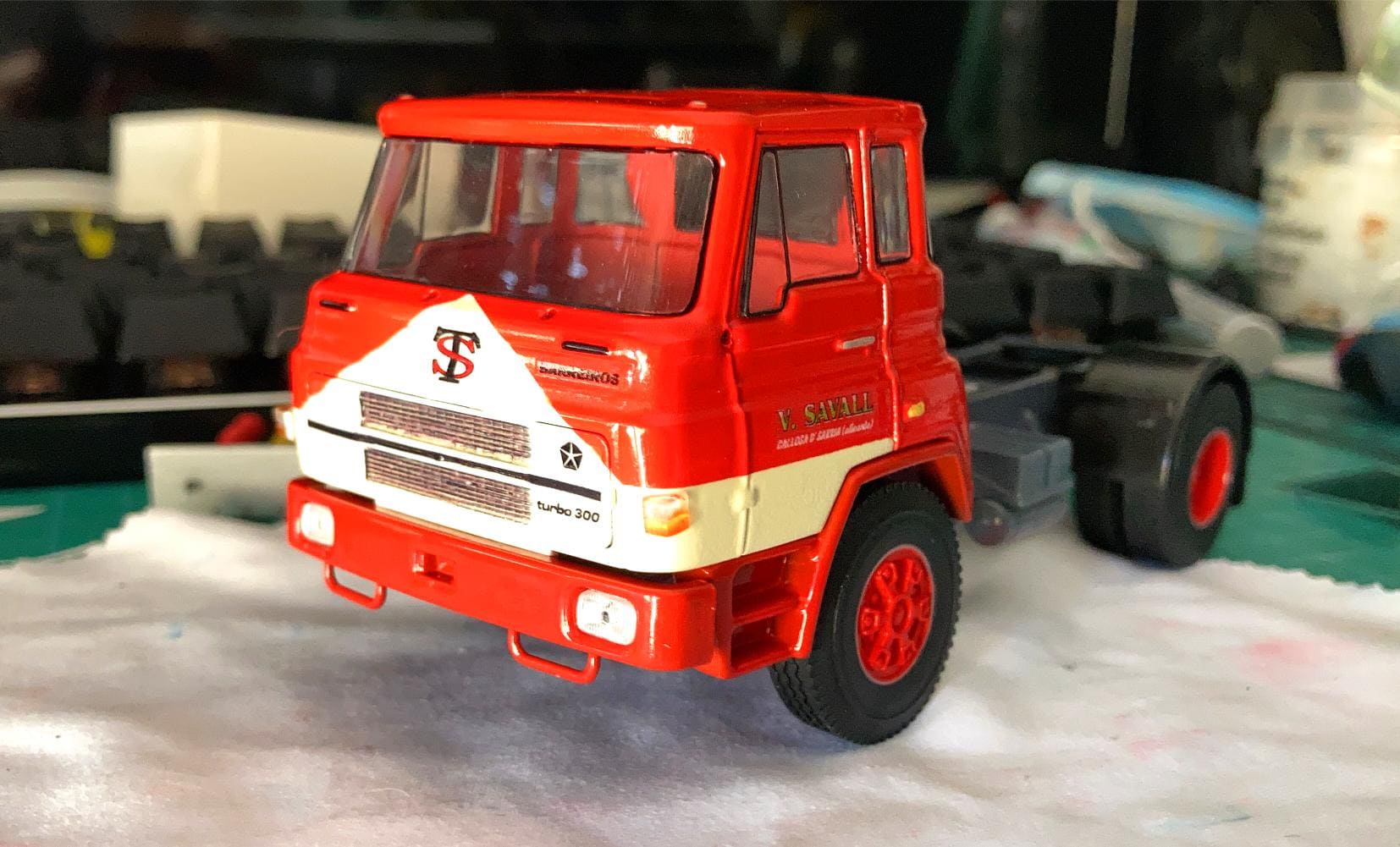 Un modelo de camión rojo con una franja blanca se encuentra sobre una mesa, mostrando una marca detallada y elementos de diseño que recuerdan el viaje de Antonio Fernández superando obstáculos.
