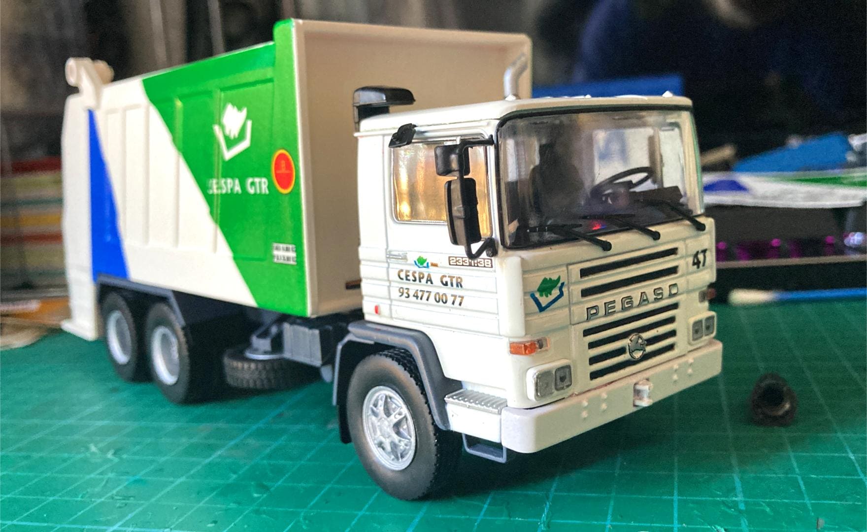 Modelo de un camión de basura Pegaso con detalles en verde y blanco sobre tapete de corte, hábilmente elaborado para sortear cualquier obstáculo en su camino.