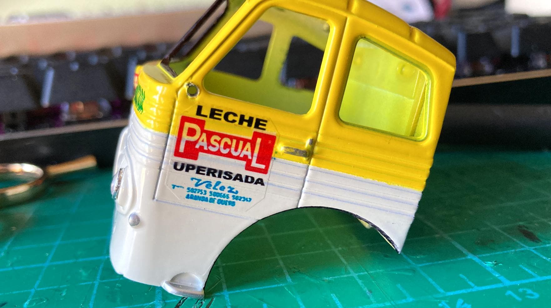 Cabina de camión de juguete amarilla con el texto "Leche Pascual" en el costado, desafiando su camino a través de una alfombra de corte, maniobrando sin esfuerzo a través de obstáculos imaginarios.