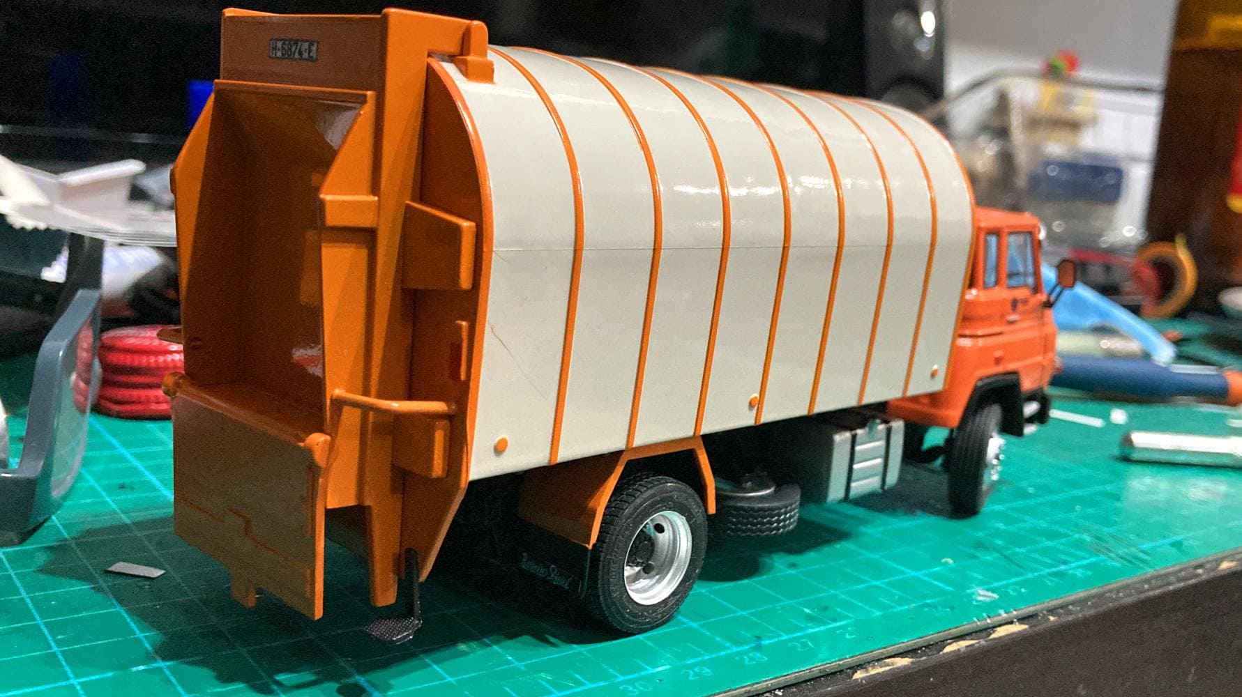 Una maqueta detallada de un camión de basura naranja y blanco avanza sobre la alfombra de corte, como si el propio Antonio Fernández hubiera considerado meticulosamente cada obstáculo potencial en el camino.
