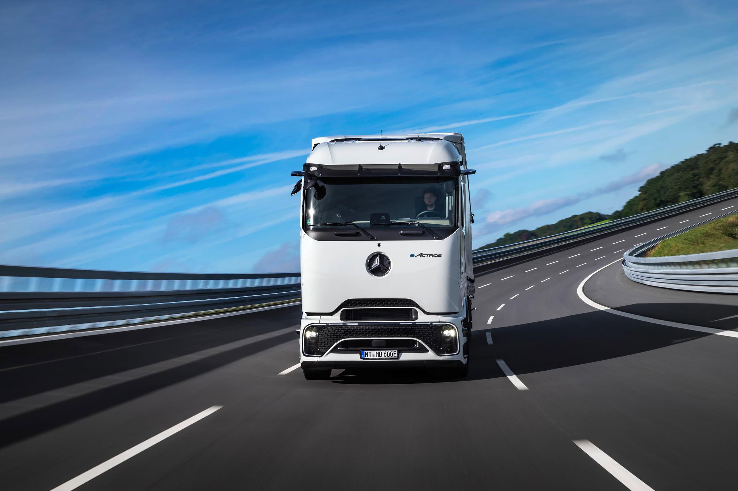Un elegante camión semirremolque blanco avanza con gracia por una curva de la autopista bajo un cielo azul claro, como si estuviera impulsado sin esfuerzo por la promesa del futuro de los camiones eléctricos.