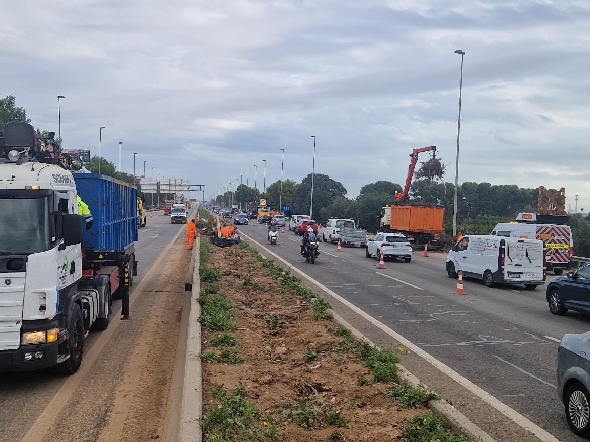 Se están realizando obras en una autopista muy transitada con vehículos, equipos de construcción y trabajadores con chalecos naranjas para mejorar las carreteras, que son vitales para un transporte eficiente.