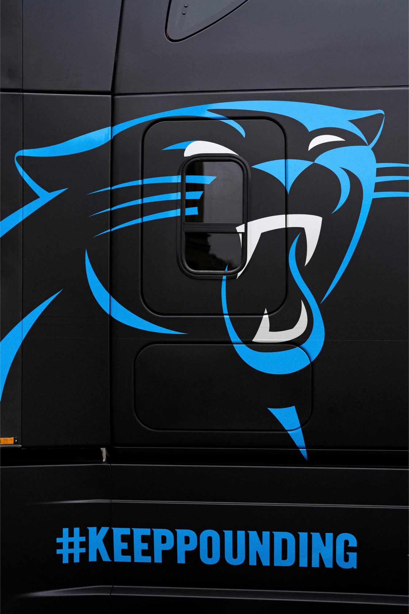 Primer plano de un camión Daimler negro con un gráfico de pantera azul y el hashtag #KeepPounding, perfecto para mostrar su orgullo por los Carolina Panthers durante el fin de semana del juego de la NFL.