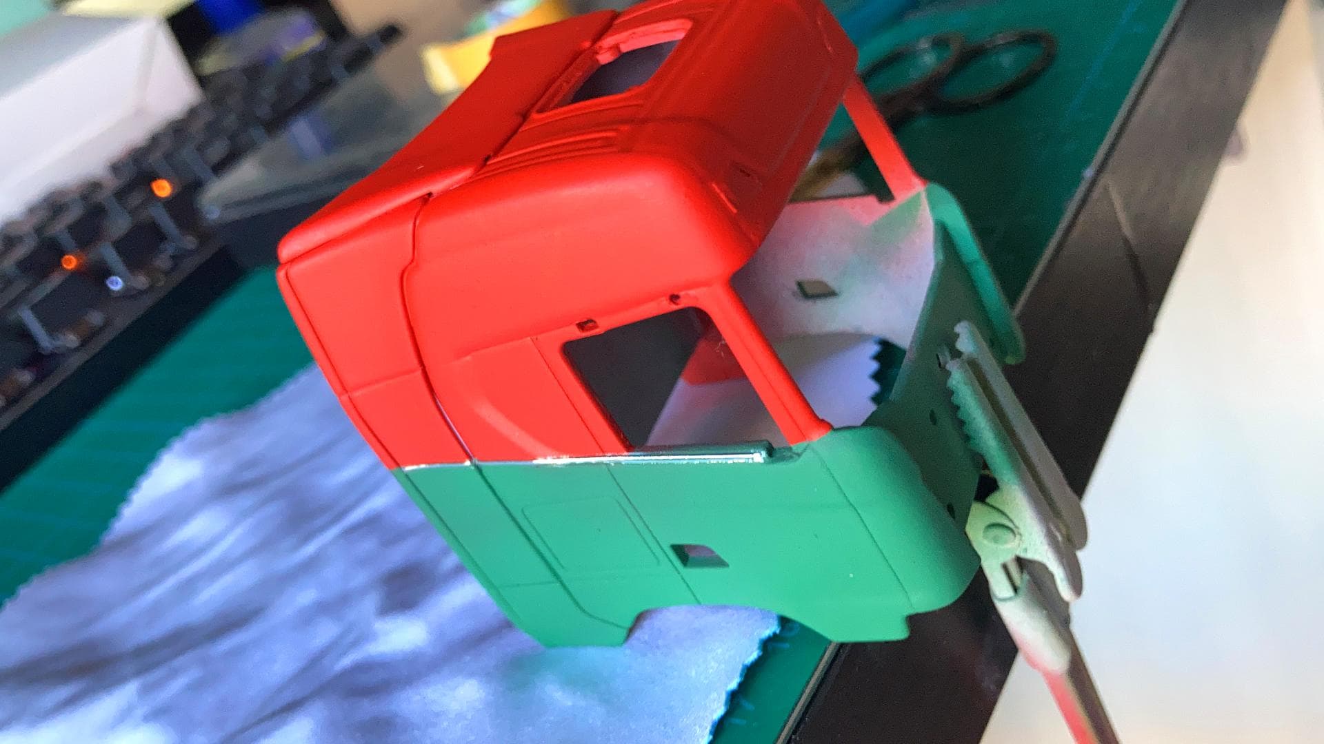 Maqueta de cabina de camión pintada de rojo y verde, colocada cuidadosamente sobre una abrazadera para pintar por Antonio Fernández, recorriendo con precisión el camino artístico, superando cualquier obstáculo a su paso.