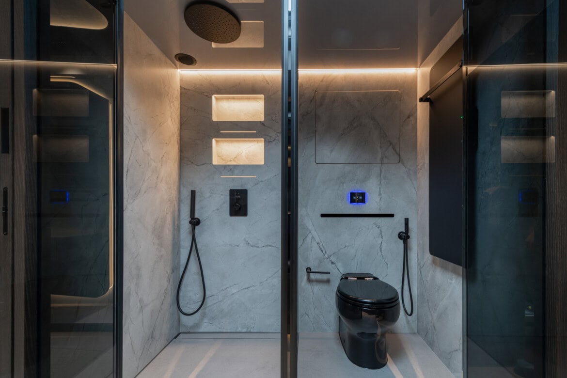 Baño moderno con elegante ducha Brabus, controles montados en la pared y un inodoro negro contra paredes de mármol.