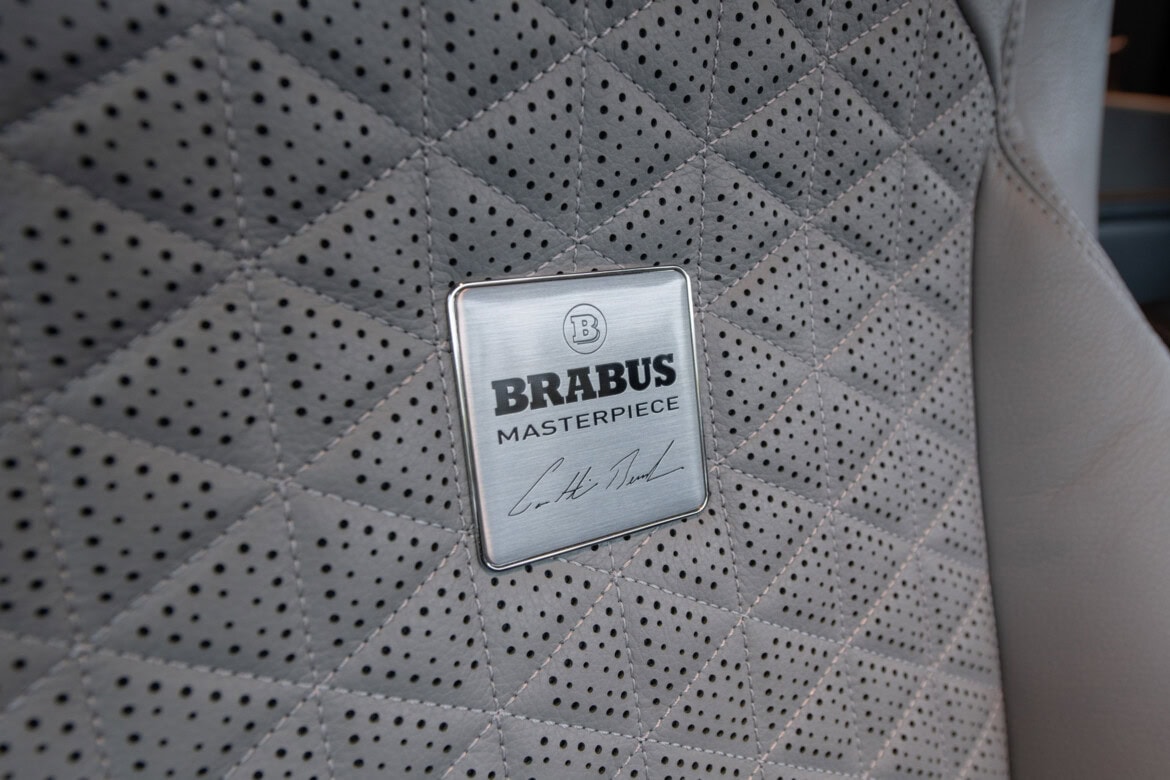 Primer plano de un asiento de automóvil con cuero gris cosido con diamantes y una placa de metal con la etiqueta "BRABUS MASTERPIECE", que hace eco del lujo extravagante del Brabus Big Boy 1200.