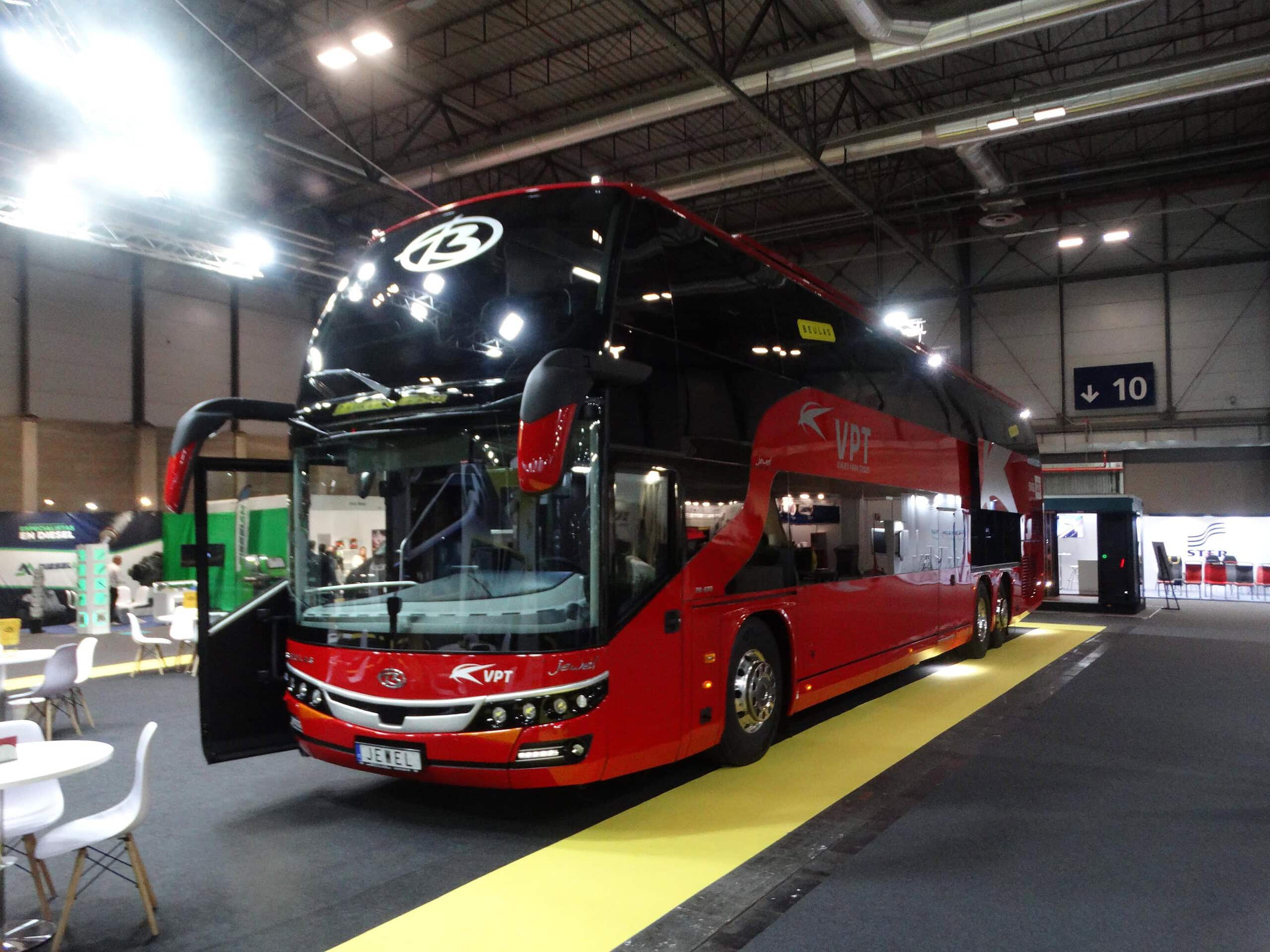 Un autobús rojo de dos pisos se exhibe en un gran espacio interior con techo alto, capturando la esencia vibrante de la Feria Internacional del Autobús.